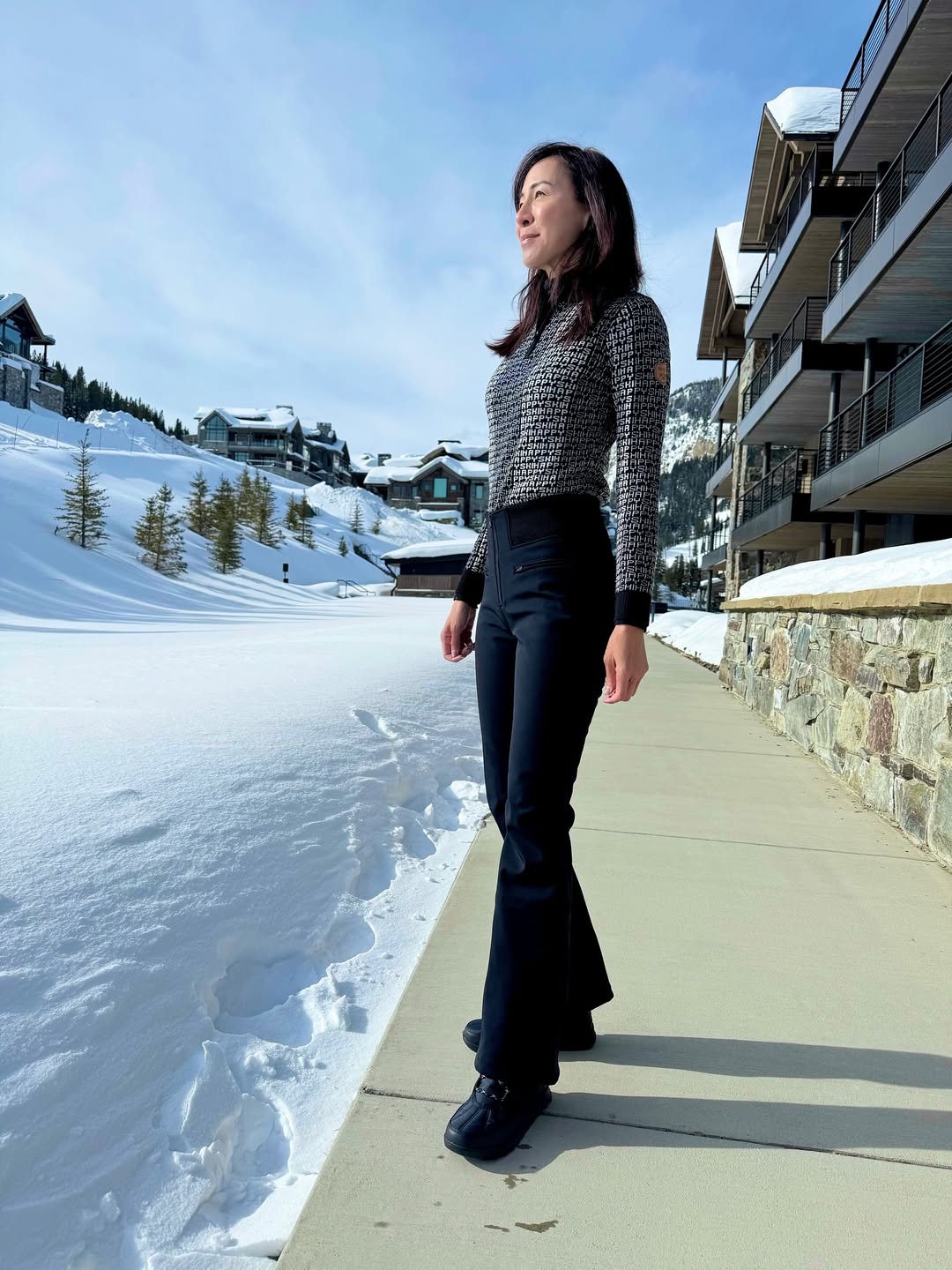 Woman in a FERA Kate Parka and sweater layers holding ski poles, enjoying a sunny day on the slopes.