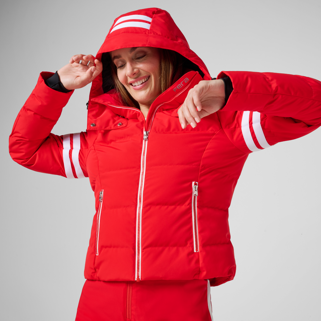 Woman wearing a red FERA Kate parka with white stripe detail and black Brooke stretch insulated bib pants for full ski coverage.
